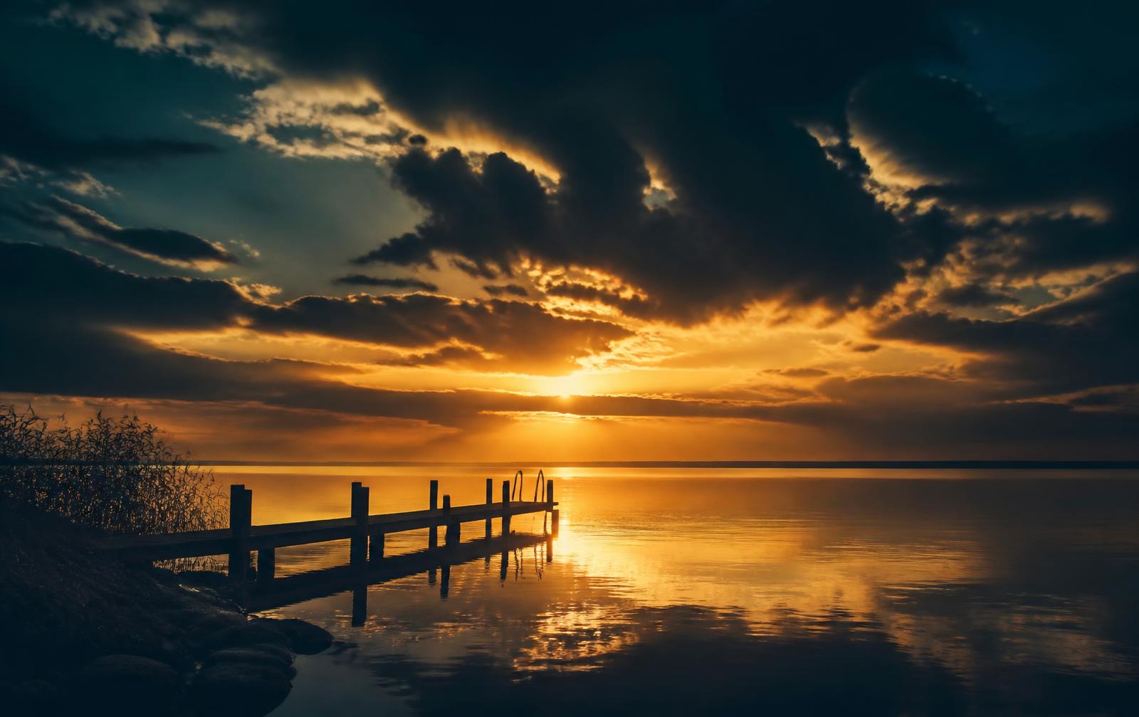 Golden light breaking through storm clouds over calm water at sunrise